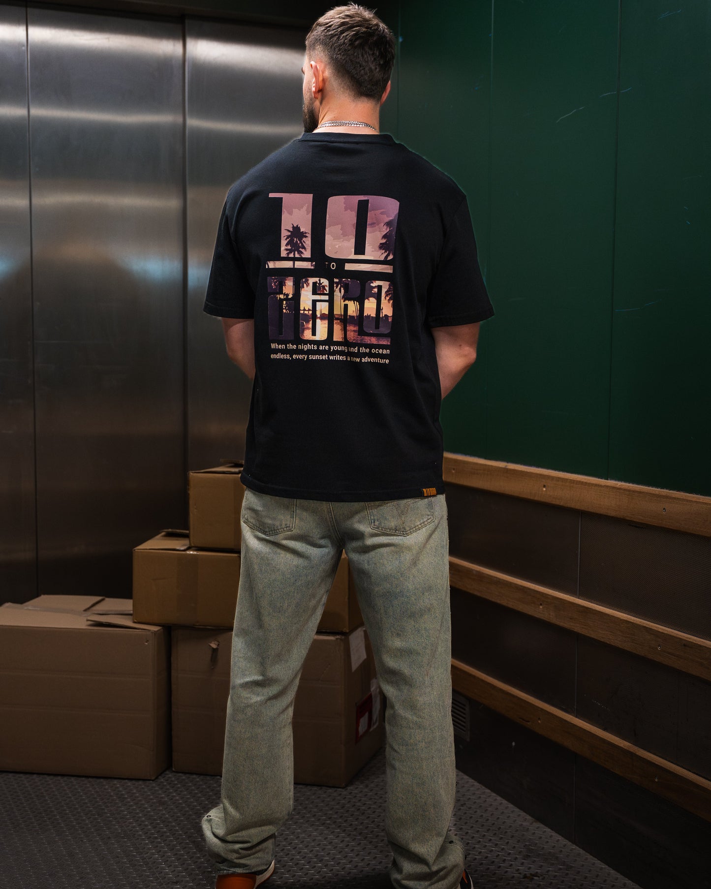 Sunset Adventures Tee in Black – back view with sunset palm tree photo fill inside 10 to Zero letters