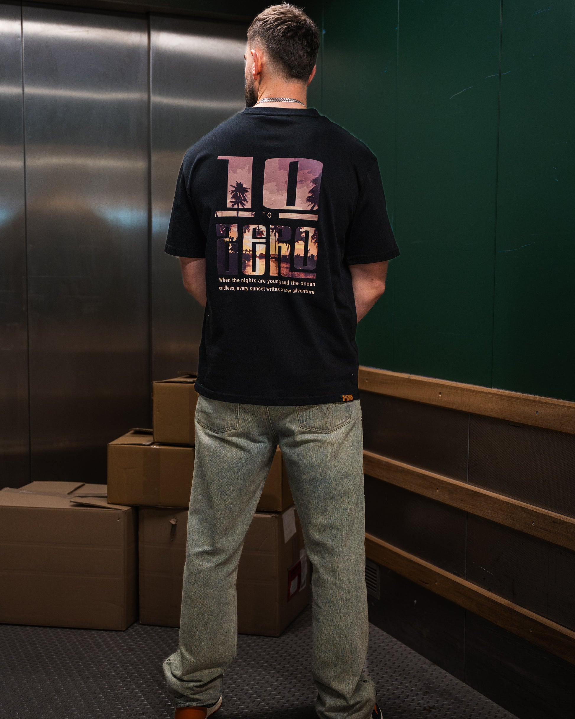 Sunset Adventures Tee in Black – back view with sunset palm tree photo fill inside 10 to Zero letters