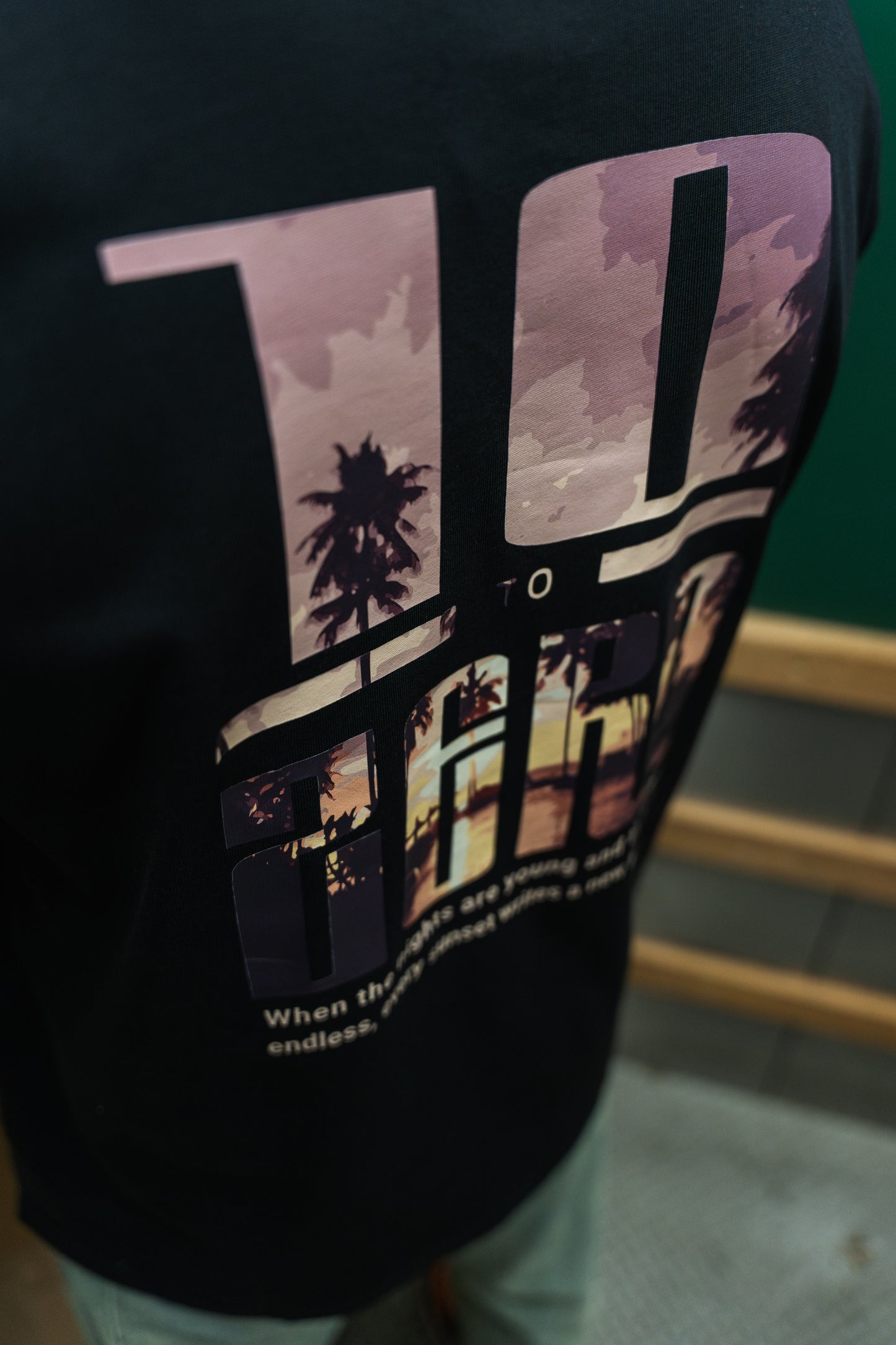 Sunset Adventures Tee in Black – back view with sunset palm tree photo fill inside 10 to Zero letters