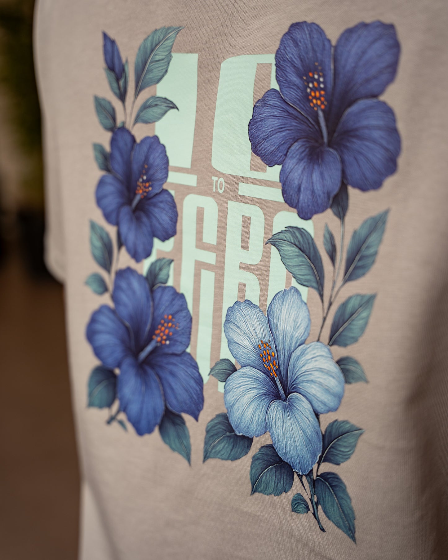Blue Sauvage Tee in Dizzle Grey – back view with blue hibiscus floral print over 10 to Zero graphic